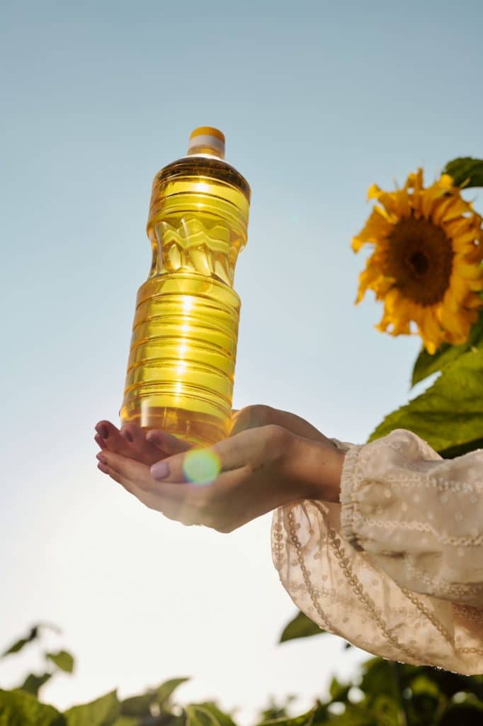 Hands of young woman in white dress holding bottle of sunflower oil